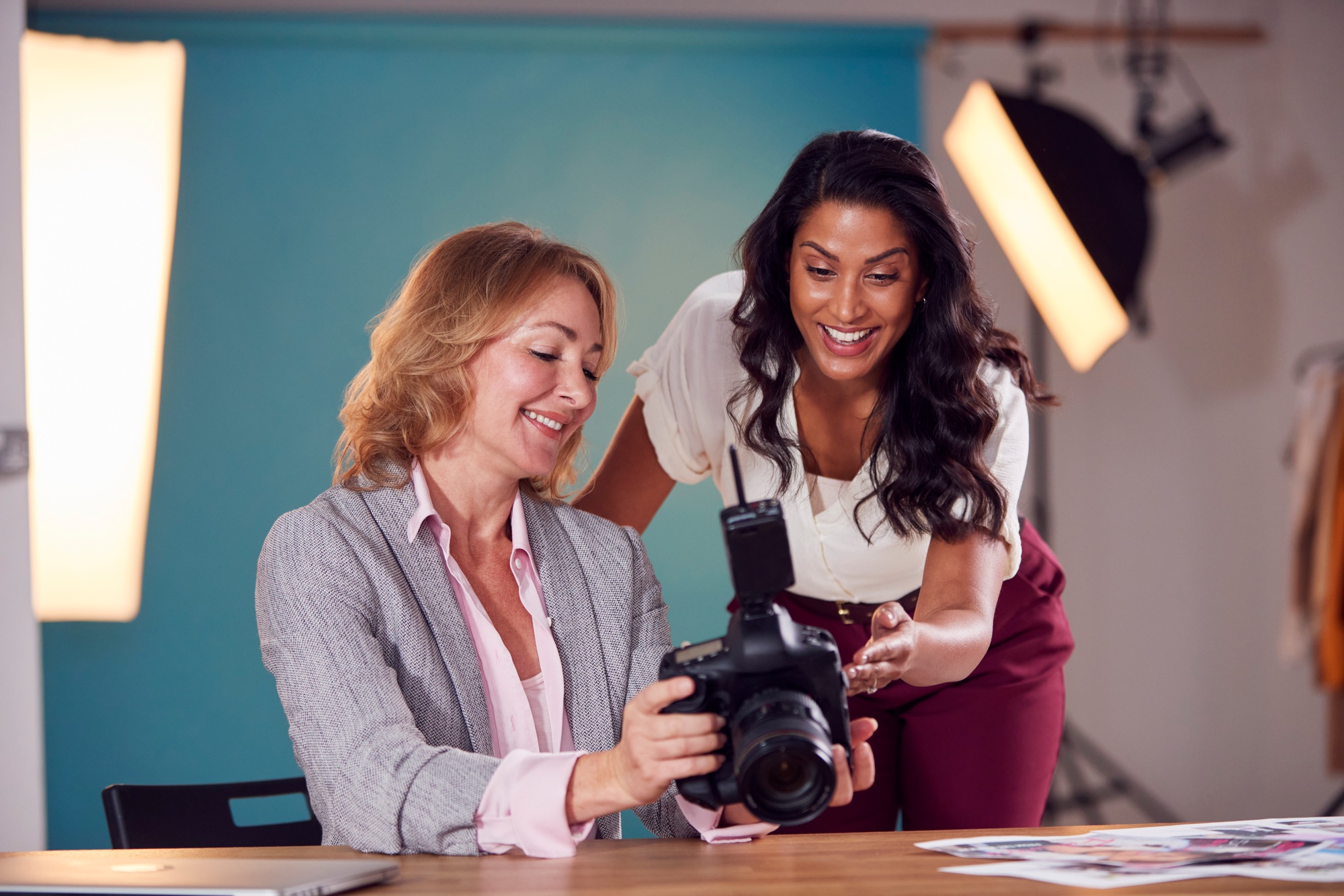 Mature Female Fashion Photographer With Client Looking At Images From Shoot On Camera In Studio