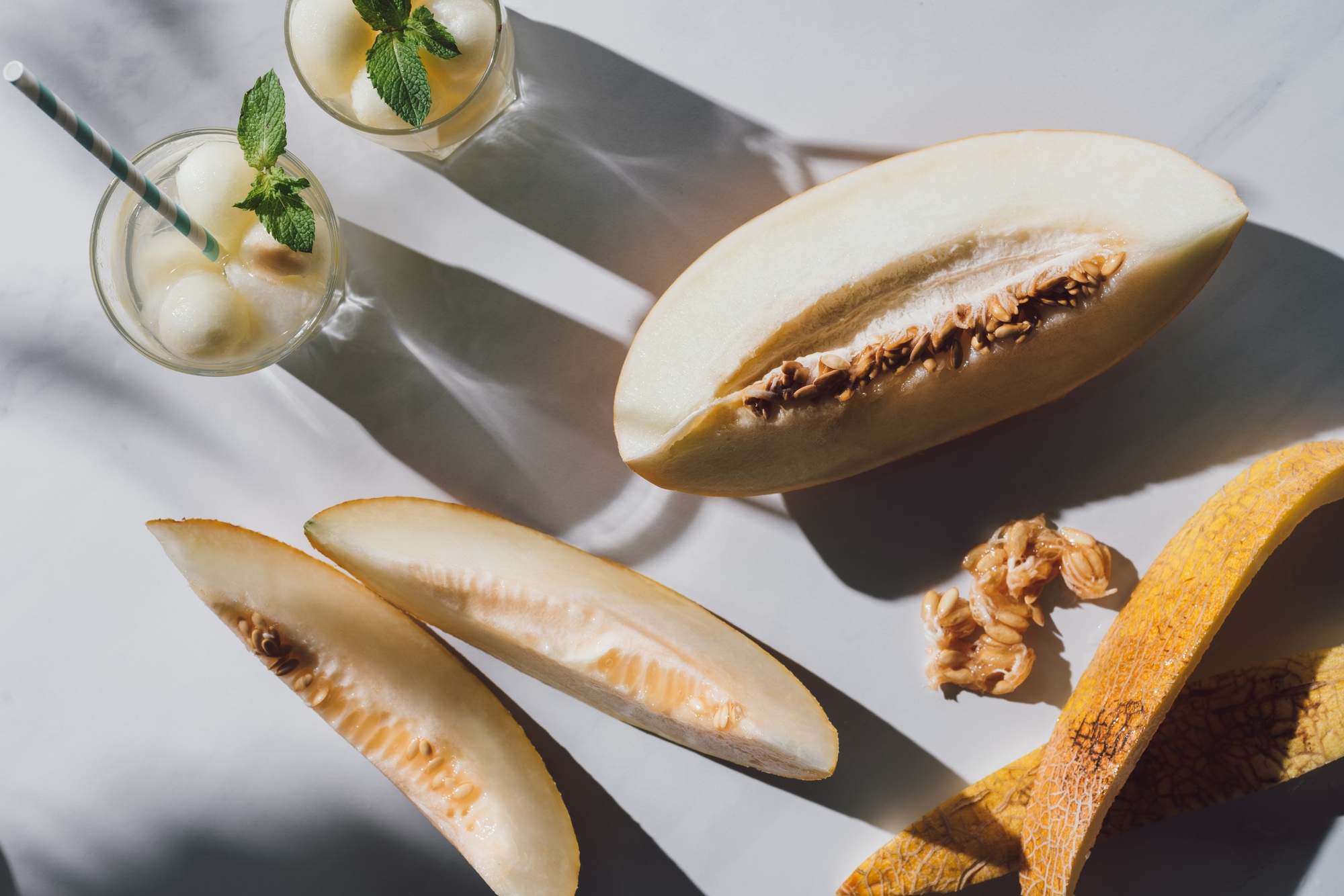top view of delicious ripe melon, glasses with refreshing beverage and seeds on white