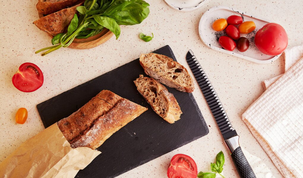 Preparing of traditional caprese salad with fresh tomatoes, basil, mozzarella and baguette.