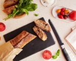 Preparing of traditional caprese salad with fresh tomatoes, basil, mozzarella and baguette.
