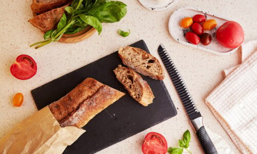 Preparing of traditional caprese salad with fresh tomatoes, basil, mozzarella and baguette.
